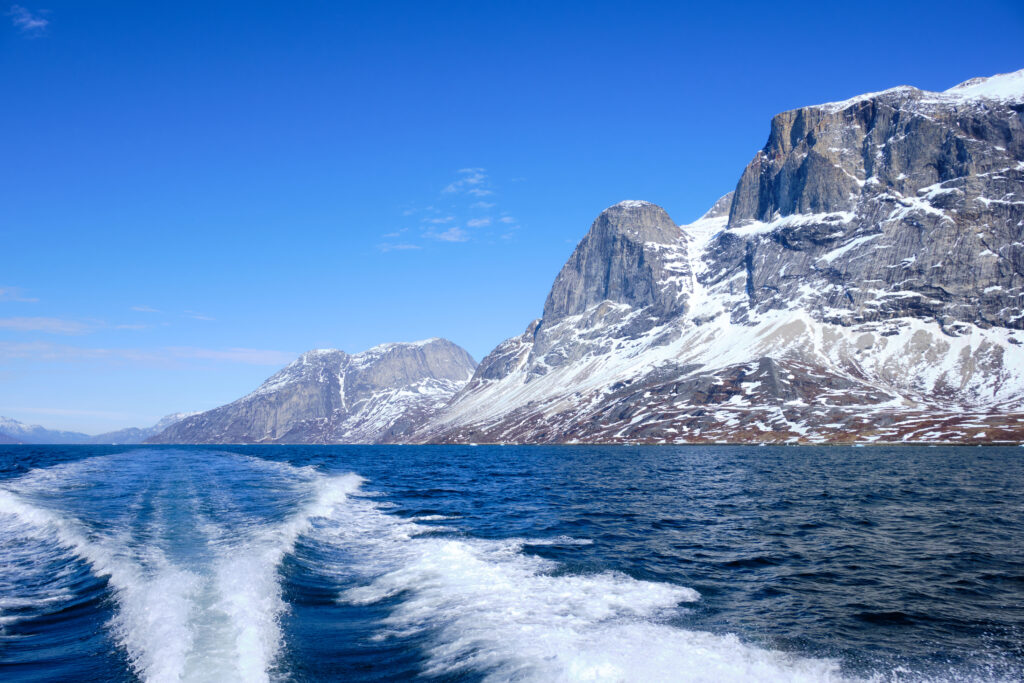 Looking back along the wake of the boat at the impressive mountains of the Nuuk fjord on a boat tour to Qooqqut with Guide to Greenland