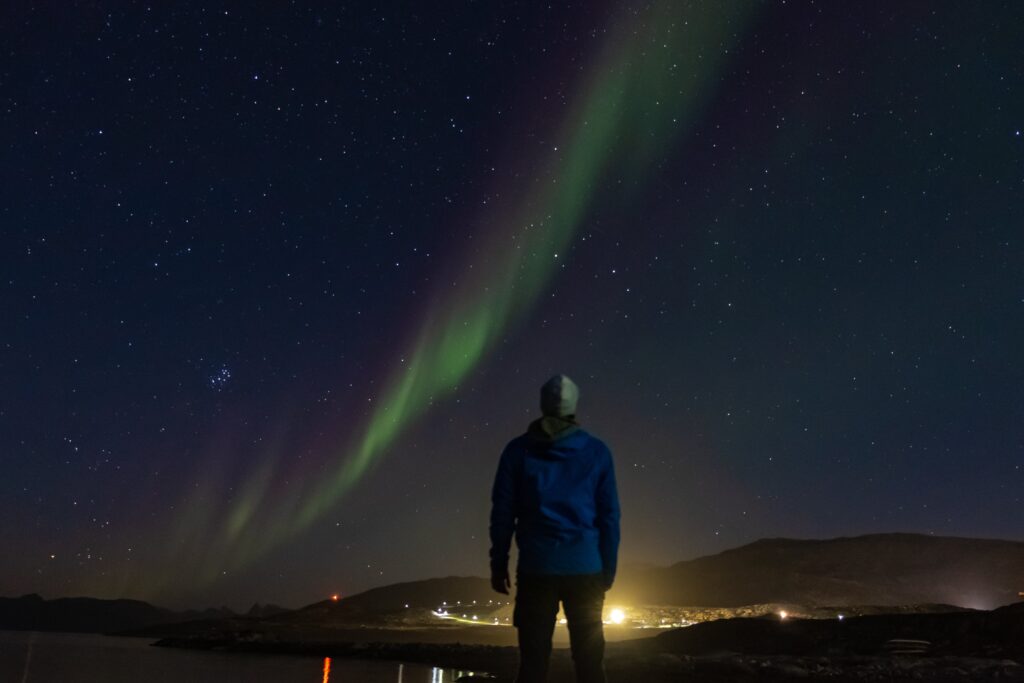 A man adoring the northern lights in the starry night sky in Greenland in winter