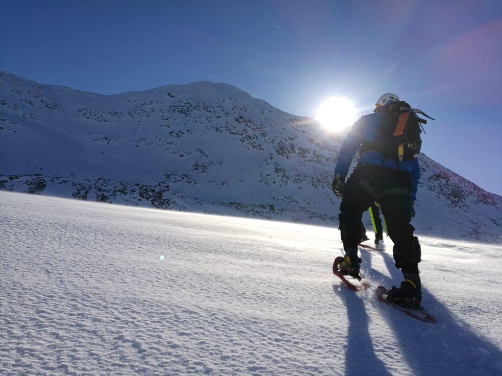 Two people snowshoeing up a hill with the sun in the background in Greenland during winter