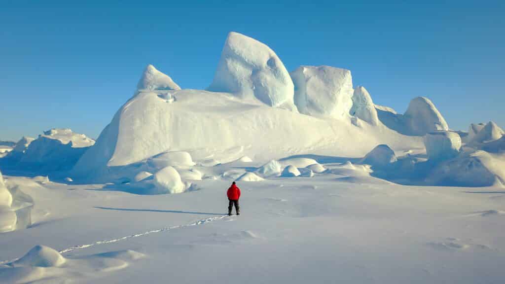 Man in a red coat looking towards a large iceberg
