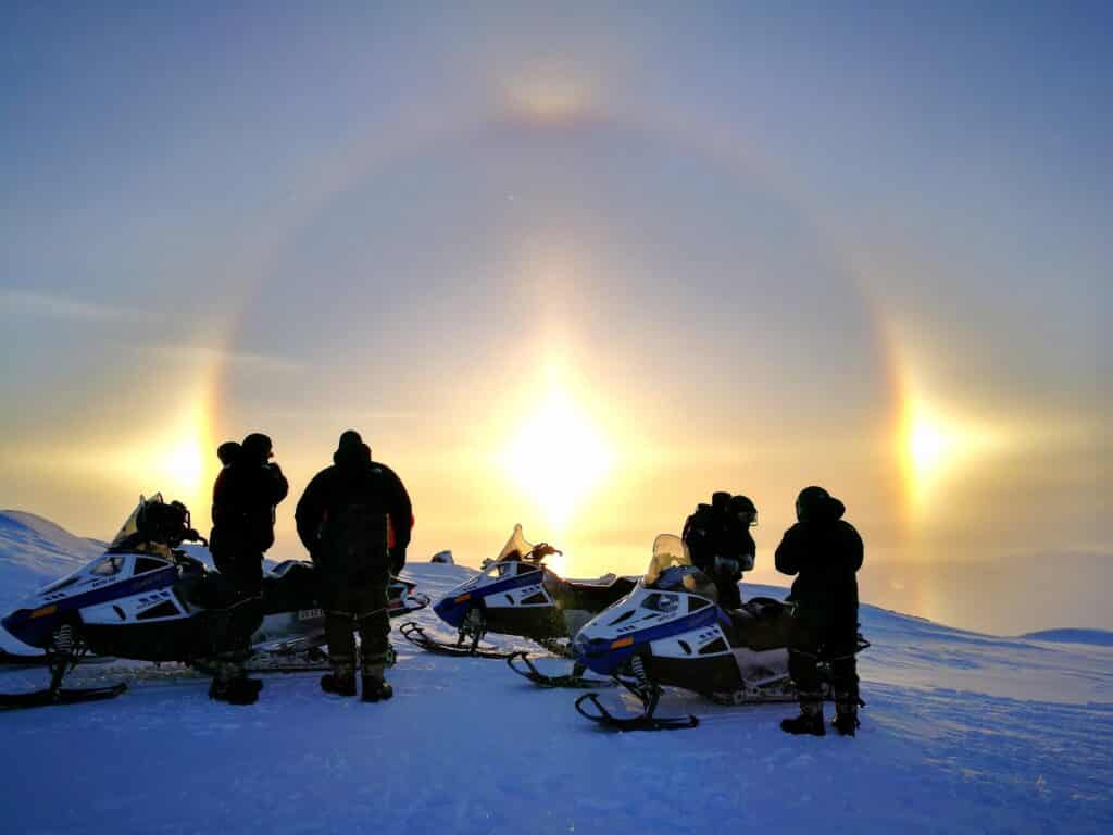 Group of people on snowmobile looking towards a beautiful sunset