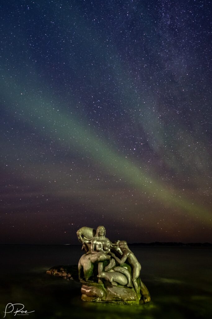 Northern lights over a statue in the water