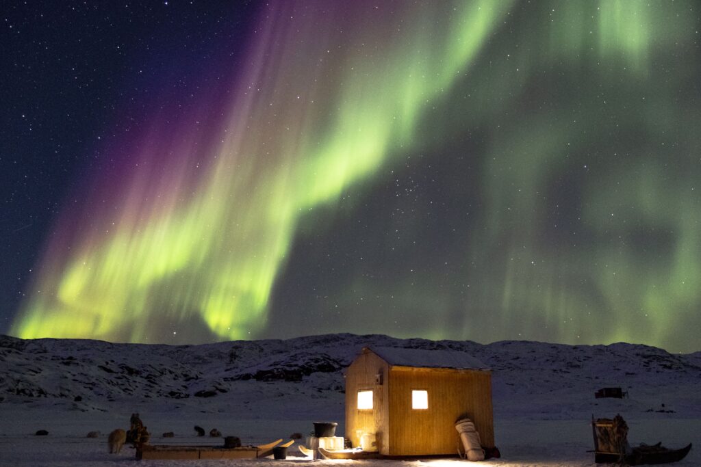 Green and purple northern lights over a small hut
