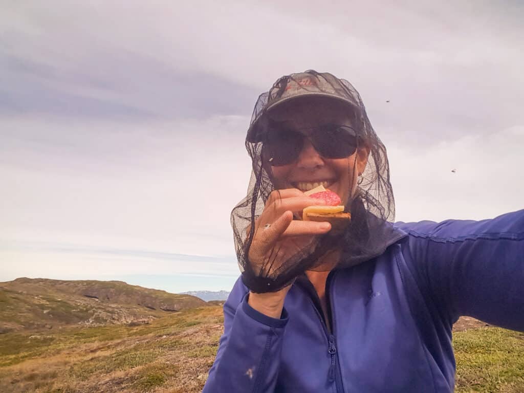 Hiker eating while wearing a head net during a hike in the Summer in Greenland