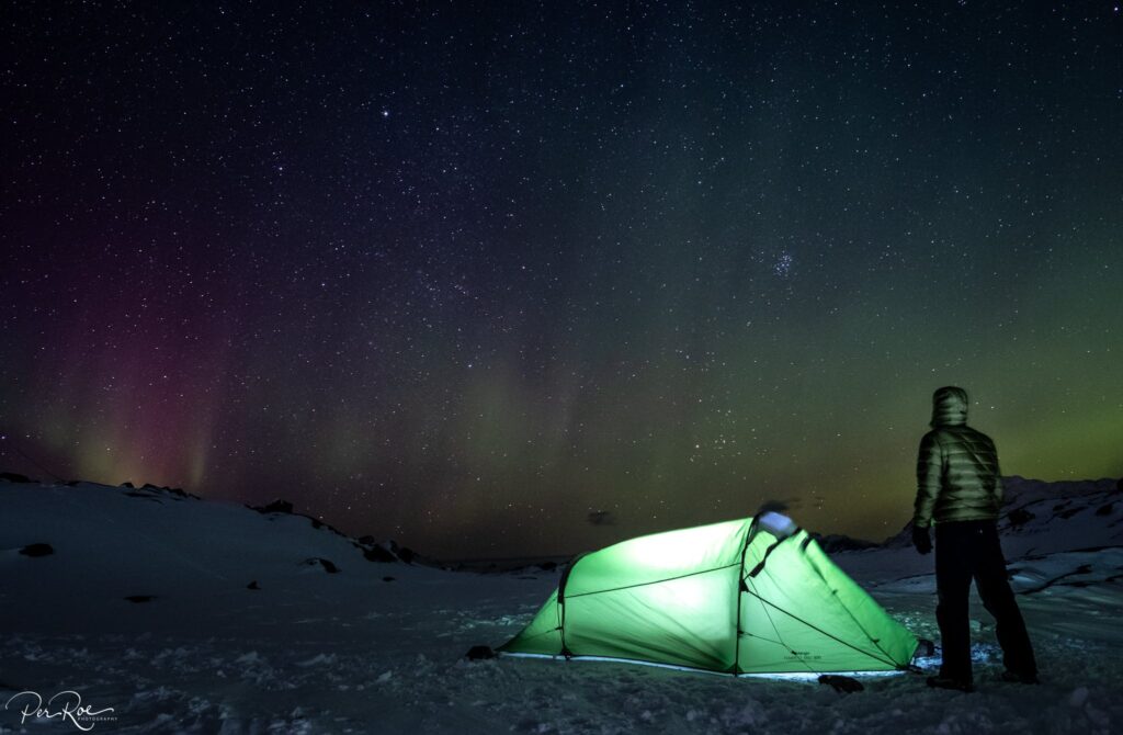 Guys next to a green tent looking at the northern lights