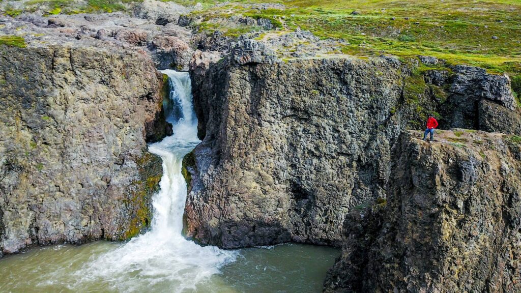 Man in red coat looking towards a waterfall in the Disko Bay in Greenland