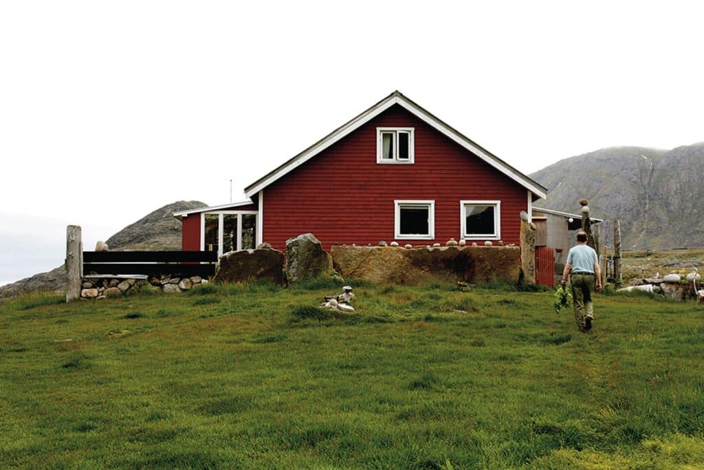 Man walking towards a red house in the south of Greenland