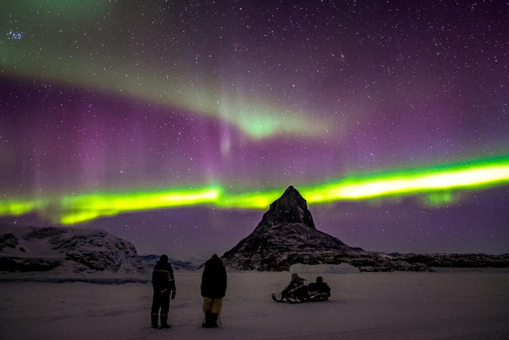 Couple riding on snowmobile and watching the northern lights in Greenland