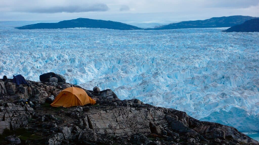 An orange tent next to a large glacier in Greenland