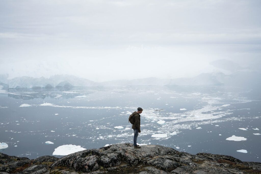 Man at the top of a mountian with icebergs in the back
