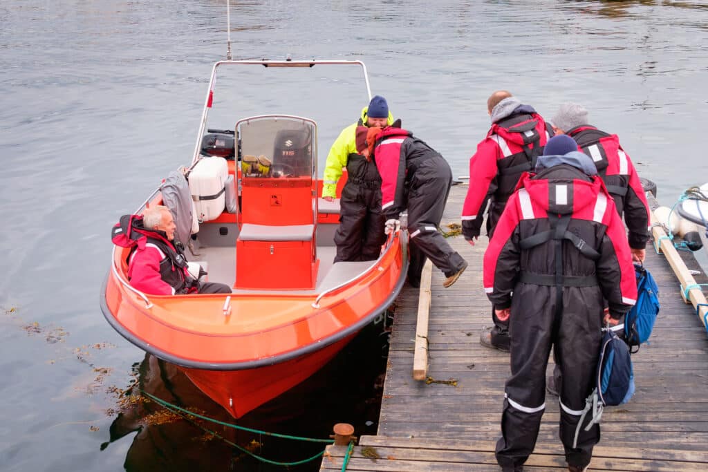Guests in flotation suits boarding an open boat in Aasiaat